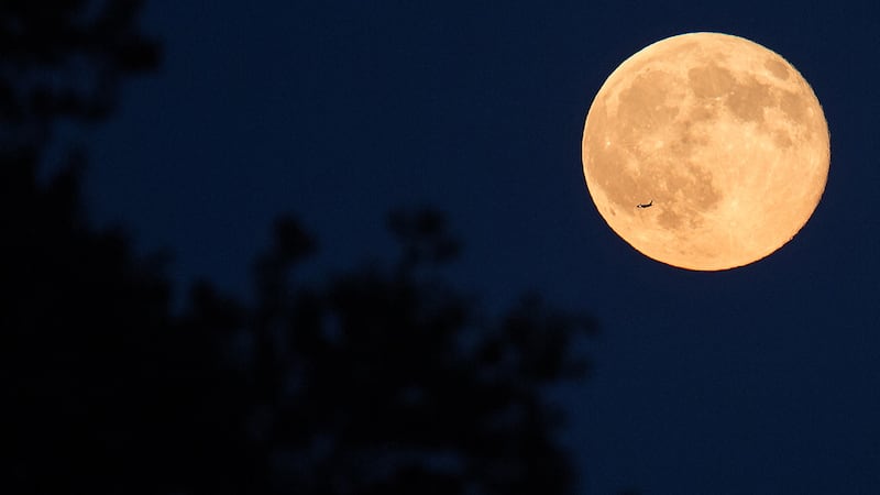 A plane passes in front of a full moon in Arlington, Virginia.